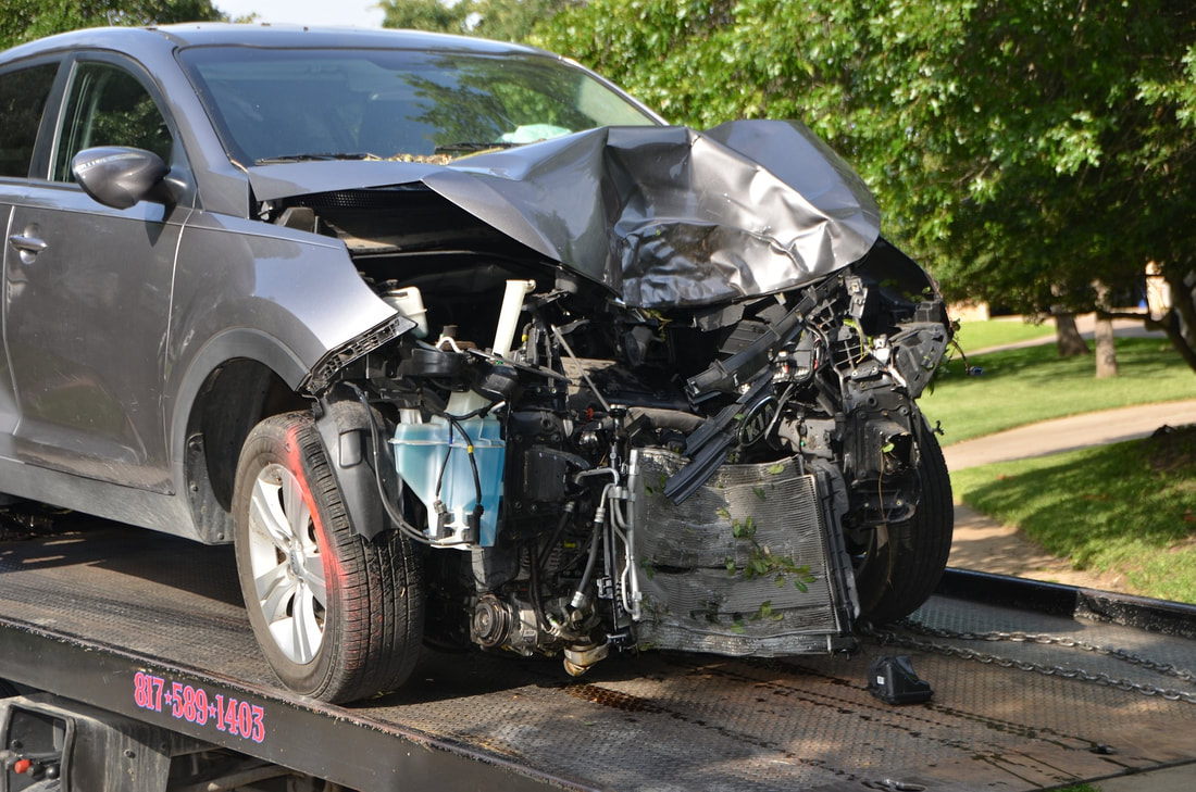 Car wrecked and loaded on the back of a tow truck trailer, exemplifying the need for vehicle liability coverage.